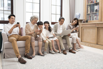 Happy Chinese family using digital devices on sofa