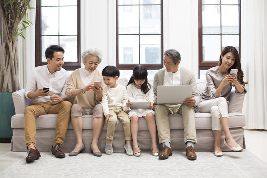 Happy Chinese Family Using Digital Devices On Sofa