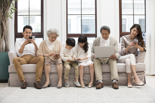 Happy Chinese family using digital devices on sofa