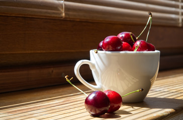 Cherry berries in a white cup on a wooden background with a light from the window