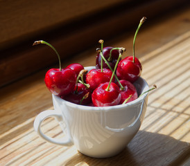 Cherry berries in a white cup on a wooden background with a light from the window