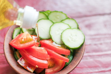 Adding vegetable oil to a salad of fresh tomatoes and cucumbers.