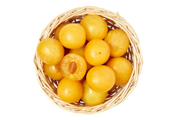 Yellow cherry plums also known as mirabelle plums in woven basket isolated on white background. Top view