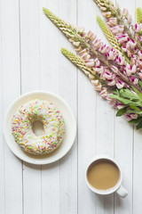 Still life with a Cup of coffee and lupine flowers donut Notepad on a light wooden table. Copy space