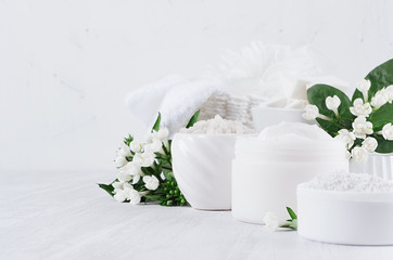 Fototapeta na wymiar Luxury pure white cosmetics set of natural products for body and skin care - cream, salt, scrub and small flowers as border on white wood board, closeup.