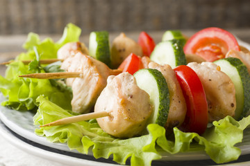 Traditional chicken kebab on wooden skewers with tomatoes, cucumbers and fresh herbs on a plate.