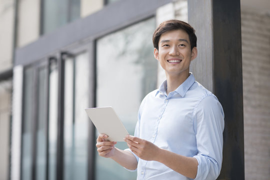 Young Chinese businessman holding a digital tablet outdoors