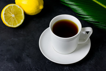 Obraz na płótnie Canvas A cup of tea, a sliced lemon and a green leaf on a dark background