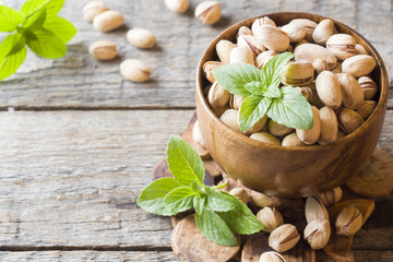 Delicious salted pistachios and fresh mint leaves on wooden background