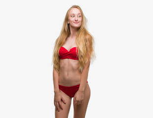 Blonde teenager woman wearing red bikini smiling looking side and staring away thinking.