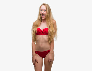 Blonde teenager woman wearing red bikini afraid and shocked with surprise expression, fear and excited face.