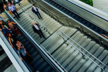 People on stairs and moving escalator at the interchange station near business and commercial...