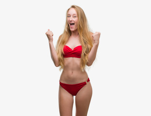 Blonde teenager woman wearing red bikini celebrating surprised and amazed for success with arms raised and open eyes. Winner concept.
