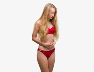Obraz premium Blonde teenager woman wearing red bikini with hand on stomach because nausea, painful disease feeling unwell. Ache concept.