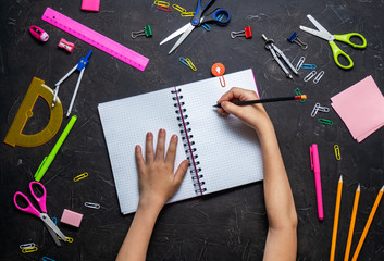 Back to School: Stationery and children's hands on a dark table.
