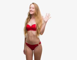 Blonde teenager woman wearing red bikini showing and pointing up with fingers number five while smiling confident and happy.