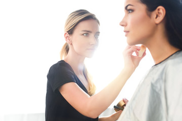Naklejka premium selective focus of beautiful young woman getting makeup done by focused makeup artist