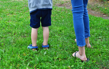 Fototapeta na wymiar Children legs younger brother and older sister together walking outdoors in yard in green grass background in summer day. Family and friendship concept.