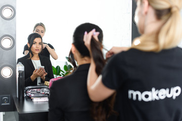 selective focus of hairstylist doing hairstyle for businesswoman with smartphone