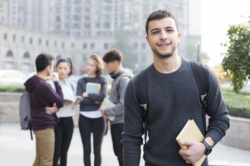 Cheerful male abroad student on campus with his friends in background