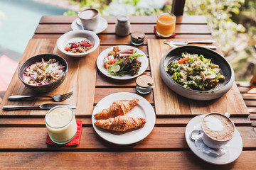 Breakfast for two on wooden table. Croissants, fresh salad, natural juice, coffee, yoghurt with granola and fruits