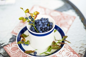 Bleberries in cup and plate on glass table.