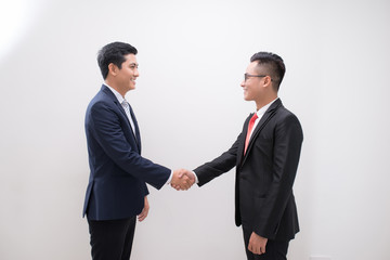 Side view of two smiling young businessmen shaking hands in white background