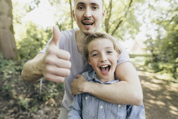Portrait of happy young man embracing boy on forest path