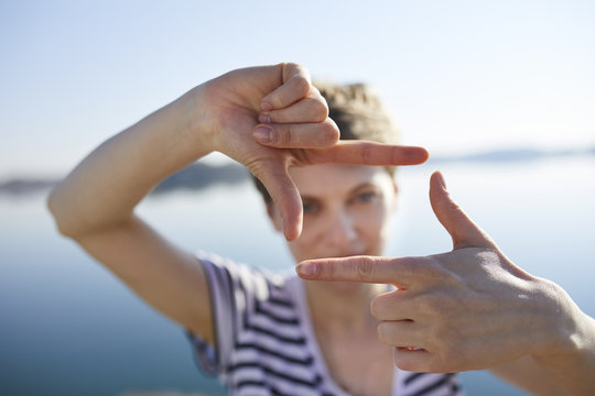 Woman in front of lake shaping frame with her fingers, close-up