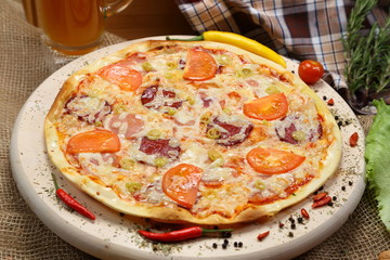Pizza with tomato, cheese, smoked sausage, boiled sausage, pepper spices on a wooden tray close-up