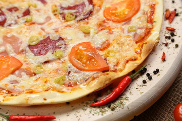 Pizza with tomato, cheese, smoked sausage, boiled sausage, pepper spices on a wooden tray close-up