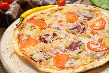 Pizza with tomato, cheese, smoked sausage, boiled sausage, pepper spices on a wooden tray close-up