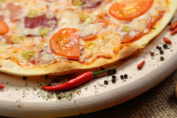 Pizza with tomato, cheese, smoked sausage, boiled sausage, pepper spices on a wooden tray close-up