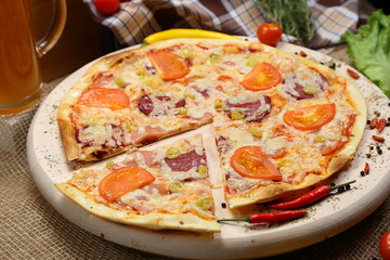 Obraz na płótnie Canvas Pizza with tomato, cheese, smoked sausage, boiled sausage, pepper spices on a wooden tray close-up