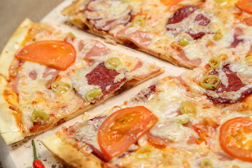 Pizza with tomato, cheese, smoked sausage, boiled sausage, pepper spices on a wooden tray close-up