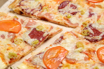 Pizza with tomato, cheese, smoked sausage, boiled sausage, pepper spices on a wooden tray close-up