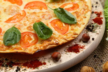 Pizza with tomato, cheese, salad, on a wooden stand closeup
