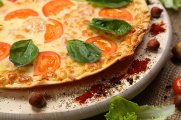 Pizza with tomato, cheese, salad, on a wooden stand closeup