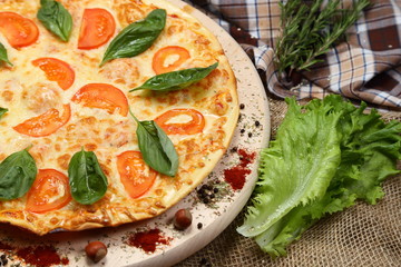Pizza with tomato, cheese, salad, on a wooden stand closeup