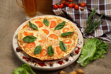 Pizza with beer in a glass mug with tomato, cheese, salad, on a wooden stand closeup