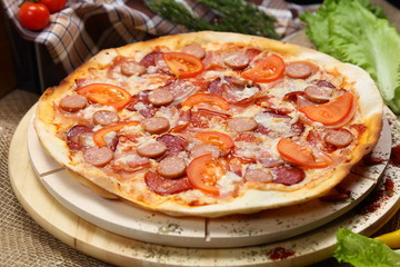 Pizza with sausages, tomato, smoked sausage, bacon, red pepper and cheese close-up