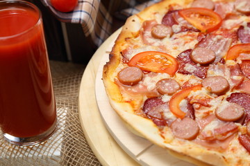 Pizza with sausages, tomato, smoked sausage, bacon, red pepper, cheese and tomato juice close-up