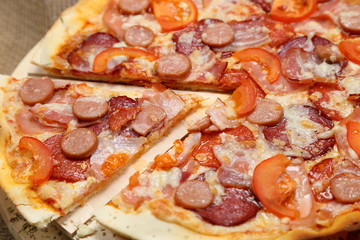 Pizza with sausages, tomato, smoked sausage, bacon, red pepper and cheese close-up