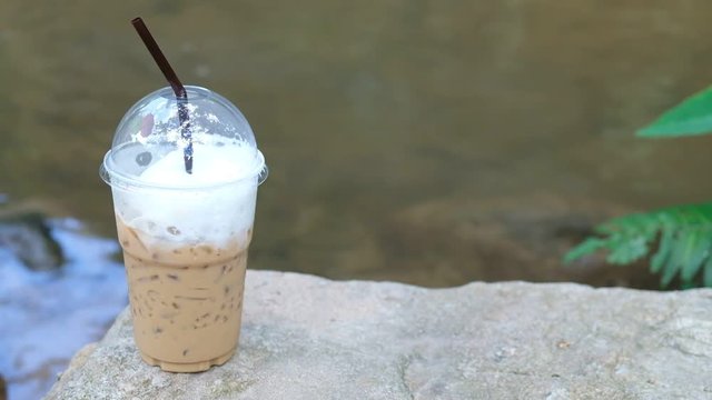 Hand picked up the iced coffee mug that was placed on the stone. The area behind the river Travel and rest, nature