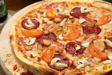 Pizza with mushrooms, tomato, smoked sausage, bacon, red pepper and cheese close-up