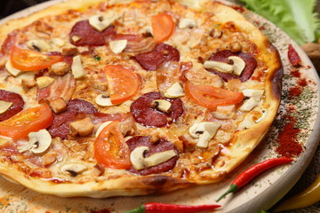 Pizza with mushrooms, tomato, smoked sausage, bacon, red pepper and cheese close-up