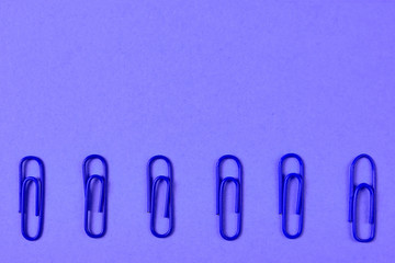 Blue paper clips isolated on violet background, close up, copy space. Top view, flat lay. Back to school, college, education concept
