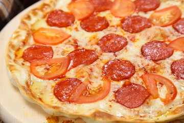 Pizza thin with smoked sausage, cheese, spices and tomatoes on a wooden stand. Cherry tomatoes and sweet peppers, lettuce leaves. Close-up