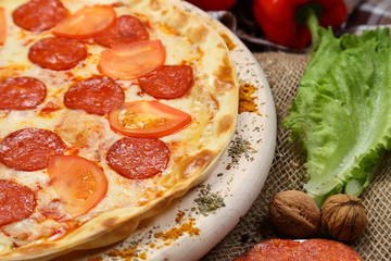 Pizza thin with smoked sausage, cheese, spices and tomatoes on a wooden stand. Cherry tomatoes and sweet peppers, lettuce leaves. Close-up