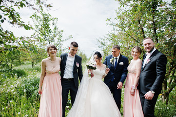 Groomsmen with bridesmaids and wedding couple posing in the garden outdoors.